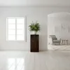 A minimalist interior scene featuring a wooden column with a floral arrangement, a window, and an archway leading to a living area with a chair and coffee table. Anteprima dell’immagine prodotto