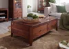 A wooden coffee table in a living room setting with a sofa and cabinets in the background. Produktbild-Vorschau