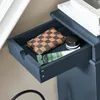 A close-up view of an open drawer in a blue cabinet, containing a checkered wallet, a tube of cream, and a small black jar. Voir les images du produit