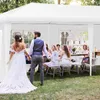 A wedding party is gathered under a white party tent, with the bride and groom in the foreground. Podgląd zdjęcia produktu