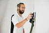 A man is sanding a wall with a power tool. Voir les images du produit