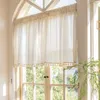 A sheer curtain with a diamond pattern and tassels hangs in a window, with greenery visible outside. Produktbild-Vorschau