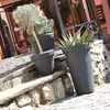 Three dark gray planters with plants are arranged on stone steps outside a building. Produktbild-Vorschau
