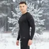 A man wearing a black long-sleeved shirt and black pants stands in a snowy forest. Náhľad obrázku produktu