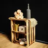 A wooden crate with two shelves, decorated with flowers, a bottle, a box, a bucket, and a book. Produktbild-Vorschau