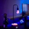 A desk setup with a lamp, headphones, and a computer monitor, illuminated by ambient blue and purple lighting. Produktbild-Vorschau