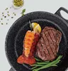 A close-up shot of a steak and lobster tail in a black granite-coated pan, garnished with lemon and rosemary, with green beans at the bottom. Some pistachios are scattered around the pan. Produktbild-Vorschau