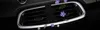A black Mr&Mrs Fragrance Cesare car air freshener is clipped onto a car's air vent, surrounded by purple flowers and green leaves. Produktbild-Vorschau
