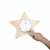 The back of a star-shaped LED night light is shown, with a finger pressing a button on the battery compartment. Náhled obrázku produktu