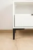A close-up view of the bottom part of a white cabinet with a black metal leg. Produktbild-Vorschau