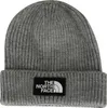 A close-up studio shot of a gray knitted beanie with a black patch featuring the North Face logo. Produktbild-Vorschau
