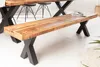 A wooden bench with black X-shaped legs is placed in a dining room setting, next to a dining table and chairs. Produktbild-Vorschau