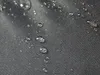 A close-up view of a black fabric surface with water droplets on it. Voir les images du produit