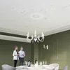 A dining room with a chandelier and two people standing near a table. Voir les images du produit