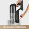 A hand is holding a black cordless vacuum cleaner, with another hand pressing a button on the vacuum. The vacuum's dustbin is visible and partially filled with dust. The background is plain white and light gray. Produktbild-Vorschau