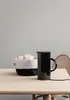 A black electric kettle sits on a wooden table next to a basket of bread. Produktbild-Vorschau
