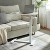 A white adjustable laptop table is positioned next to a sofa with a laptop and a cup on it. Náhľad obrázku produktu