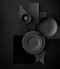A dark, abstract arrangement of plates and a bowl, suggesting a sophisticated dining or decor theme. Voir les images du produit