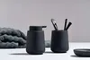 A black soap dispenser and a black cup with makeup brushes are displayed on a white surface, with a folded gray towel in the background. Produktbild-Vorschau