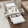 A white rectangular coffee table with multiple drawers pulled out, displaying books, boxes, and decorative items, placed on a wooden floor next to a beige sofa and a patterned rug. Produktbild-Vorschau