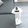 A white C-shaped side table with a cup and a smartphone on it, placed next to a gray sofa on a gray rug. Podgląd zdjęcia produktu