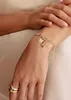 A close-up shot of a person's wrist wearing a bracelet with charms and rings. Anteprima dell’immagine prodotto