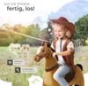 A young girl dressed as a cowboy rides a toy horse in a grassy field with trees and mountains in the background. Náhled obrázku produktu