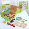 A wooden train set is displayed, partially assembled and in its packaging, on a table. Produktbild-Vorschau