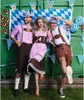 Three people in traditional Bavarian attire posing in front of a green shipping container decorated with blue and white checkered fabric and festive pennant banners. Anteprima dell’immagine prodotto