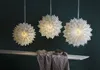 Three white paper star lanterns hang against a dark green wall, with a shelf and draped fabric in the foreground. Podgląd zdjęcia produktu