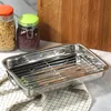 A stainless steel roasting pan with a rack sits on a checkered cloth, with jars of food and a wooden cutting board in the background. Voir les images du produit