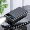 A black power bank with an LED display showing '100.' is placed on top of a black smartphone. The power bank has a flashlight emitting a bright light. Produktbild-Vorschau