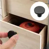 A hand is shown reaching for a black drawer knob on a wooden cabinet. Inside the drawer, an orange pot is visible. Produktbild-Vorschau