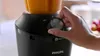 A person's hand is adjusting the dial on a black Philips blender with orange liquid inside. Náhľad obrázku produktu