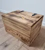 A wooden chest with a lid and black hinges sits on a wooden floor against a white wall. Náhled obrázku produktu