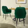 Two green velvet dining chairs are shown in a dining room setting with a wooden table. Náhled obrázku produktu