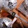 A close-up shot of a silver Casio watch with a black face, placed on a copper surface with disco balls in the background. Produktbild-Vorschau