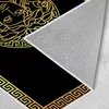 The image shows the underside of a rug with a black background and gold Greek key pattern. The rug is angled, revealing the textured backing. Produktbild-Vorschau