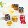 A cheese board setup with a wheel of brie cheese, a slice of cheese, and several small jars of preserves, along with fresh raspberries and a sprig of mint. Produktbild-Vorschau