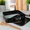 A square springform pan with a speckled black finish is shown on a kitchen counter, alongside wooden spoons and other kitchen items. Podgląd zdjęcia produktu
