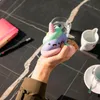 A hand holding a squishy toy unicorn on a dark marble table with a notebook and coffee cups in the background. Voir les images du produit