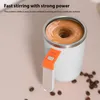 A self-stirring mug with a drink being stirred inside, placed on a light pink surface with coffee beans scattered around. Podgląd zdjęcia produktu