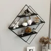 A diamond-shaped black metal wall shelf with three shelves, decorated with various decorative items, mounted on a light gray wall. Anteprima dell’immagine prodotto