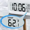 A close-up of a digital alarm clock displaying the time and temperature, with a magnified view of the temperature reading. Voir les images du produit