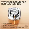 A close-up of a foundation bottle with a drop of product falling from the applicator, against a light beige background. Text overlays highlight product features. Voir les images du produit