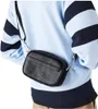 A person wearing a light blue and navy striped sweater is shown from the chest down, with a black Lacoste crossbody bag worn diagonally across their body. Náhľad obrázku produktu