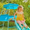 A young girl is playing on a blue and green playground set with a slide in a garden. Produktbild-Vorschau
