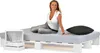 A woman sits on a pallet bed with a mattress and a pillow, next to a small white shelf unit. Produktbild-Vorschau