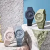 Four Casio G-Shock watches in different pastel colors are arranged on textured surfaces against a blue background. Produktbild-Vorschau