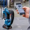 A person is holding a smartphone and interacting with an app while a cordless jigsaw is placed on a workbench. Anteprima dell’immagine prodotto